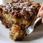 Moist German Chocolate Dump Cake topped with melted chocolate, coconut, and pecans on a white plate.